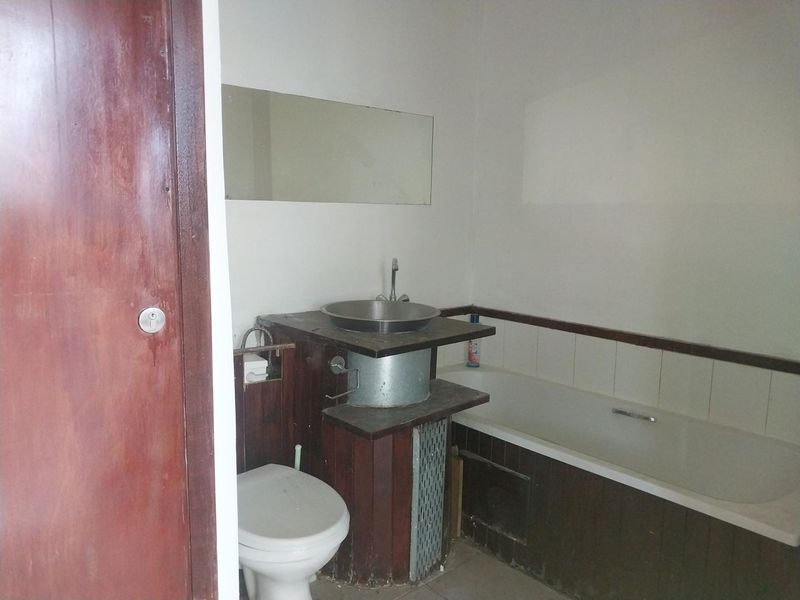 A dated bathroom featuring a built-in bathtub, a vessel sink with exposed plumbing, and a wall-mounted mirror.