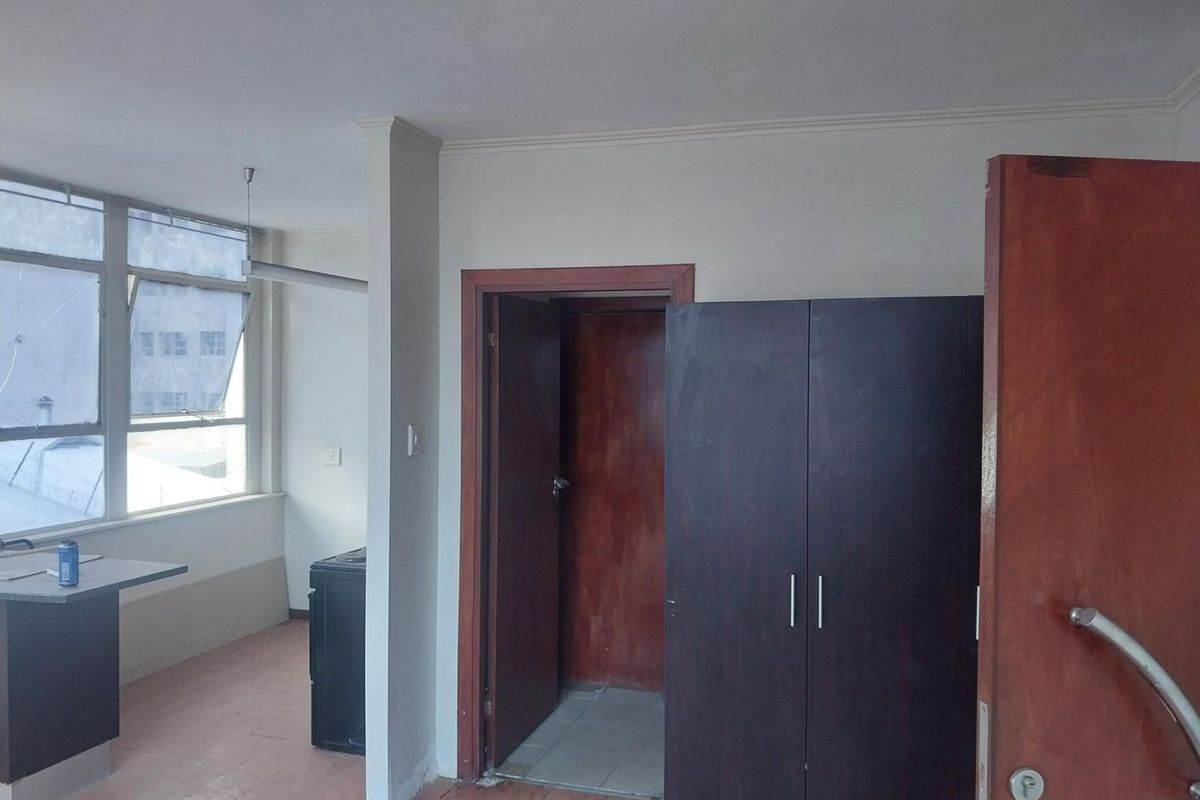A vacant bedroom featuring built-in wardrobes, large windows providing natural light, and laminate flooring, offering a blank canvas for renovation or staging.
