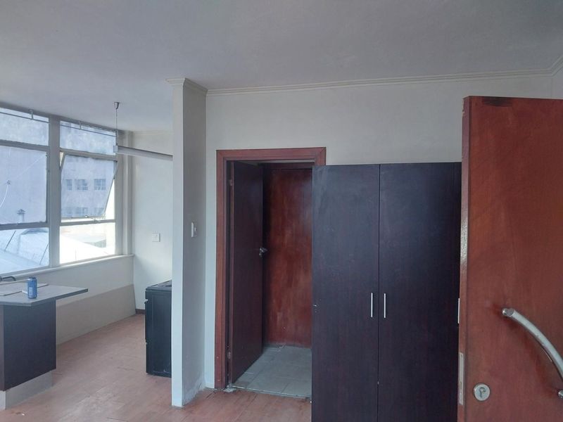 A vacant bedroom featuring built-in wardrobes, large windows providing natural light, and laminate flooring, offering a blank canvas for renovation or staging.