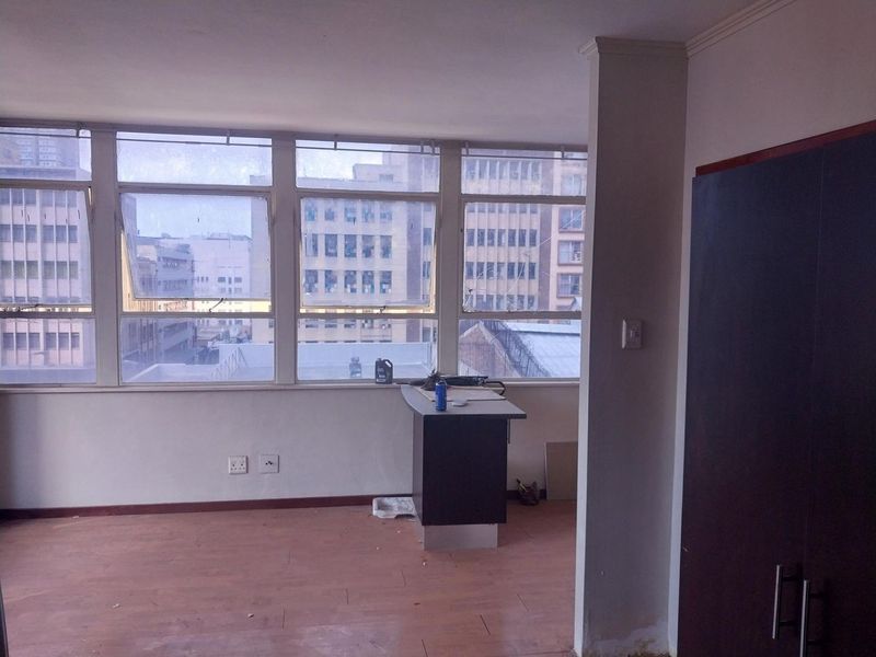 An empty living area featuring large windows with city views, laminate flooring, and a built-in cupboard, offering a blank canvas for renovation.