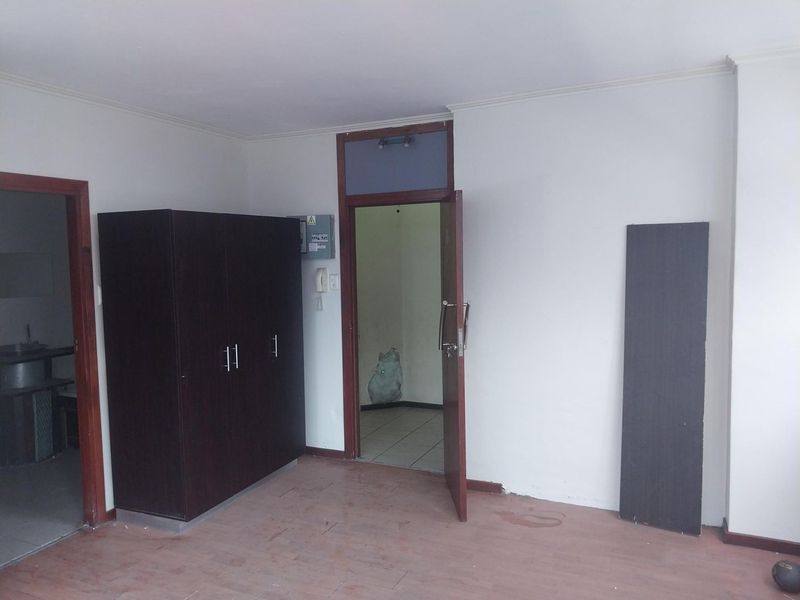 An empty living area featuring timber door frames, an intercom system, and an electrical distribution board, requiring cosmetic updates to the flooring and walls.