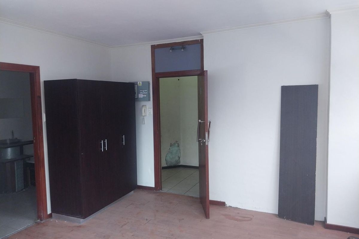 An empty living area featuring timber door frames, an intercom system, and an electrical distribution board, requiring cosmetic updates to the flooring and walls.