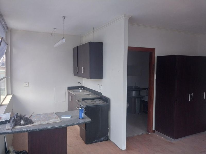 A compact kitchen area featuring dark cabinetry, a built-in stove, and a breakfast counter, adjacent to a doorway leading to another room.