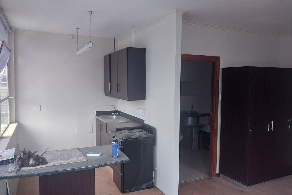 A compact kitchen area featuring dark cabinetry, a built-in stove, and a breakfast counter, adjacent to a doorway leading to another room.