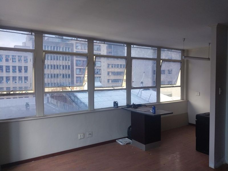An empty living area featuring a large bank of windows with city views, laminate flooring, and a fixed breakfast bar counter.