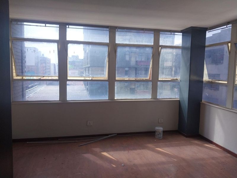 An empty living area featuring large windows with urban views, laminate flooring, and neutral walls, offering a blank canvas for renovation.