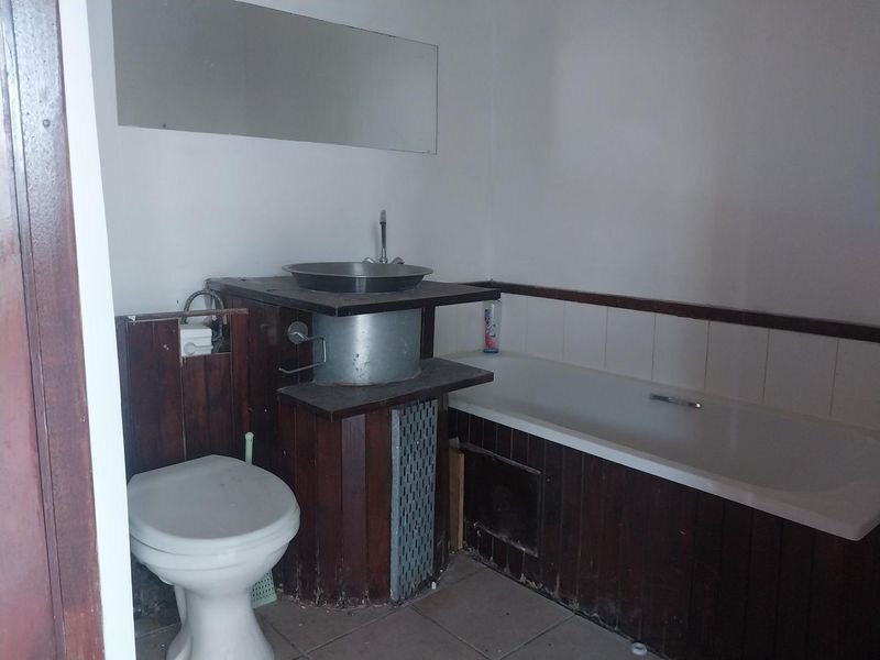 A dated bathroom featuring a bathtub, toilet, and a custom timber-clad vanity with a vessel sink, requiring modernization and cosmetic updates.