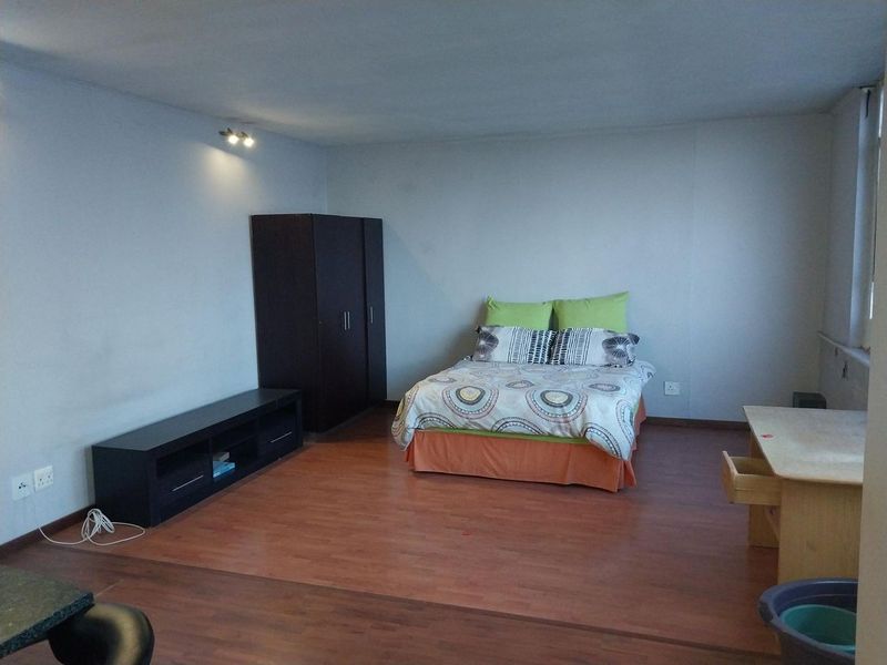 A spacious bedroom featuring laminate flooring and neutral wall finishes, providing a functional and versatile living space.