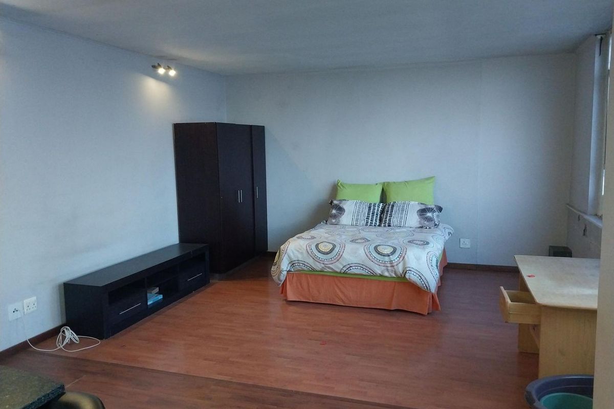 A spacious bedroom featuring laminate flooring and neutral wall finishes, providing a functional and versatile living space.