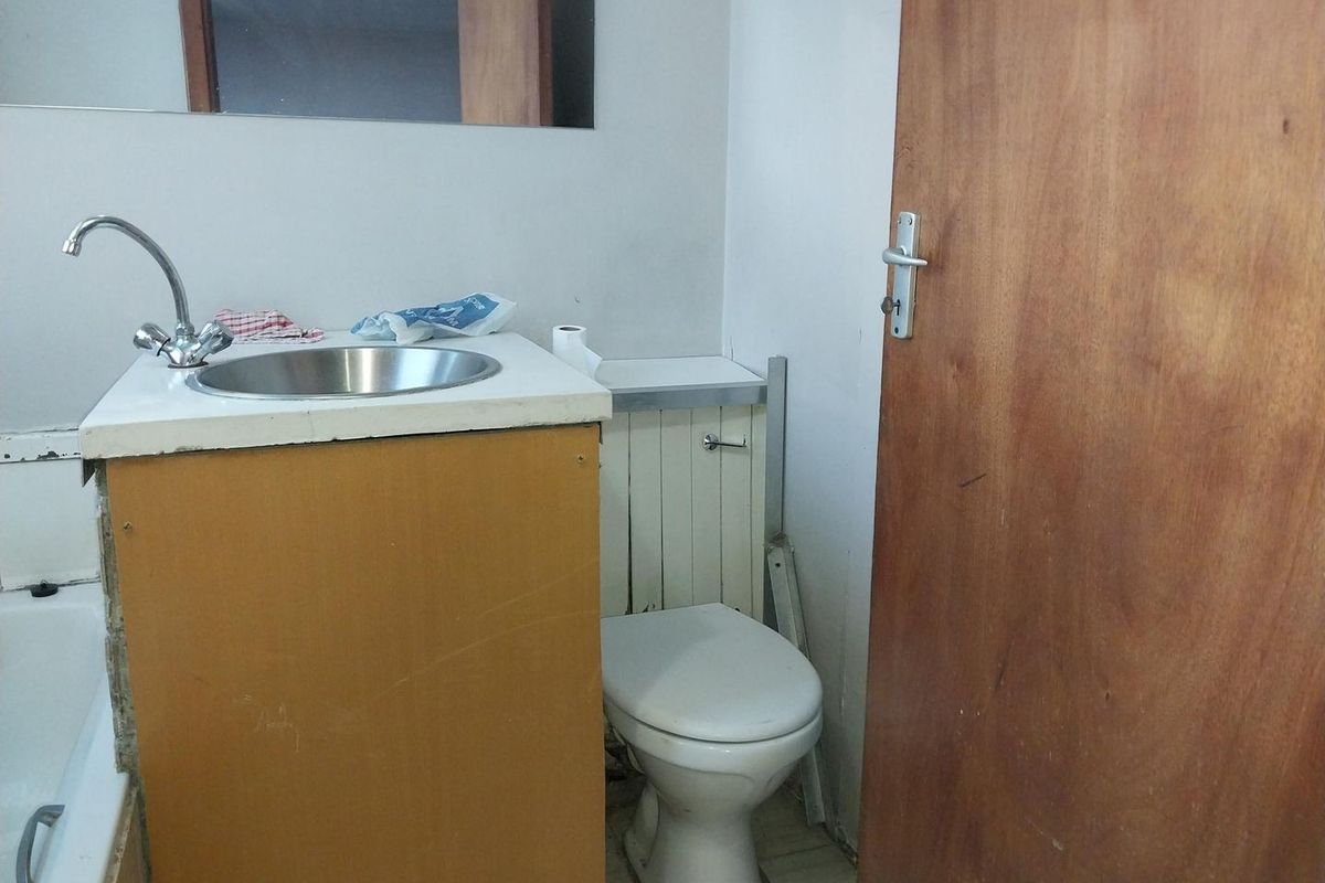 A functional bathroom featuring a vanity with a stainless steel basin, a toilet, and a bathtub, requiring cosmetic updates to improve its overall condition.