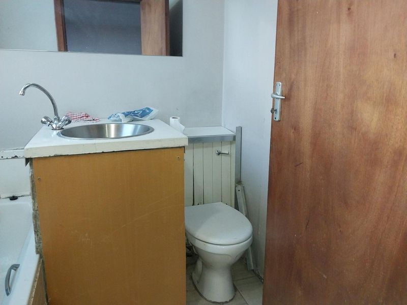 A functional bathroom featuring a vanity with a stainless steel basin, a toilet, and a bathtub, requiring cosmetic updates to improve its overall condition.