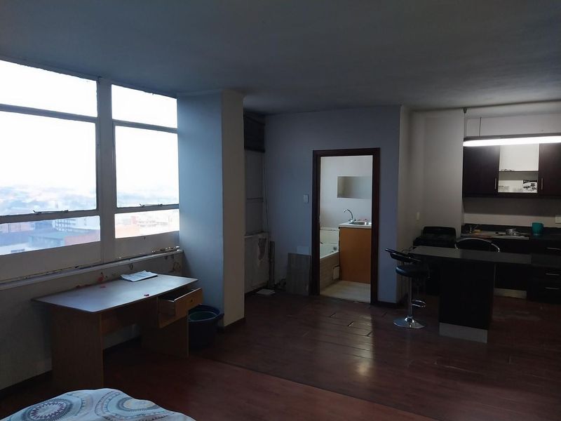 Open-plan living area featuring laminate flooring, large windows with city views, and an integrated kitchen with dark cabinetry and a breakfast island.