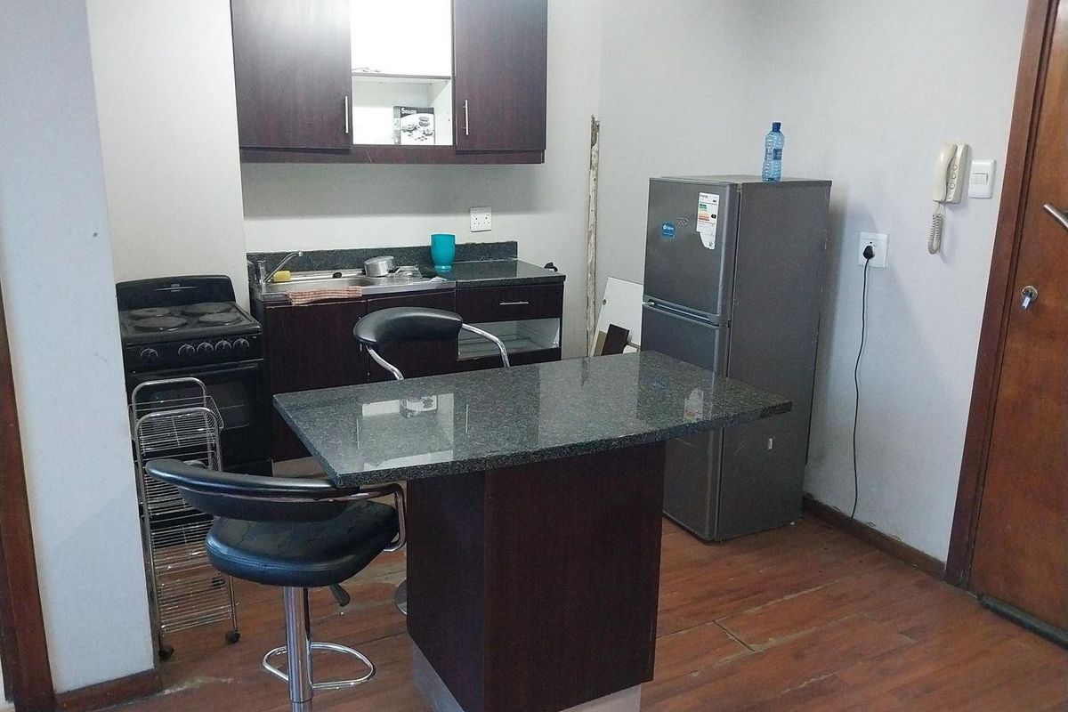 Compact kitchen featuring dark wood cabinetry, granite countertops, a breakfast bar island, and a freestanding stove, with some visible wear to the flooring.
