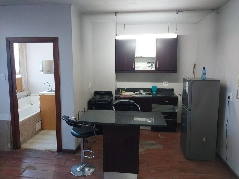 Open plan kitchen area featuring dark cabinetry and granite countertops, with an adjacent bathroom visible through the doorway. Flooring shows significant wear.