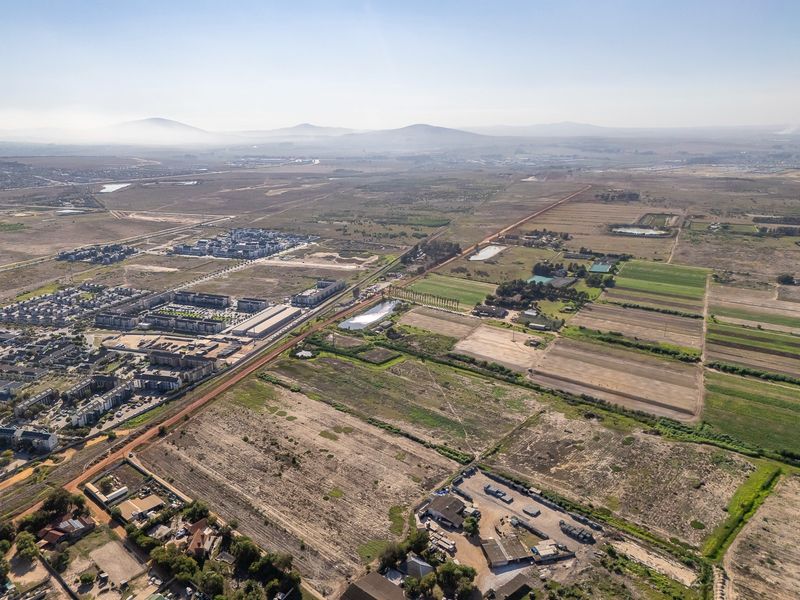 An aerial view of a large vacant land parcel situated near existing residential developments and open landscape.