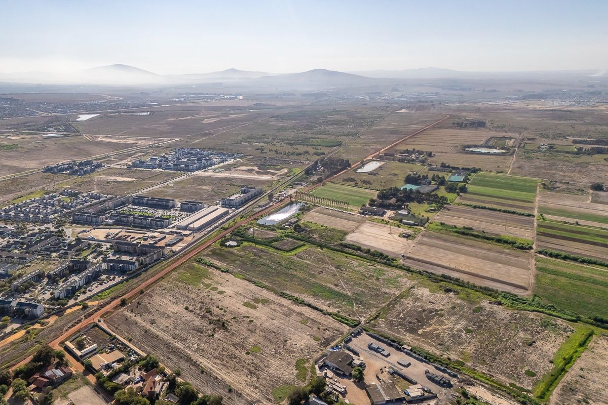 An aerial view of a large vacant land parcel situated near existing residential developments and open landscape.
