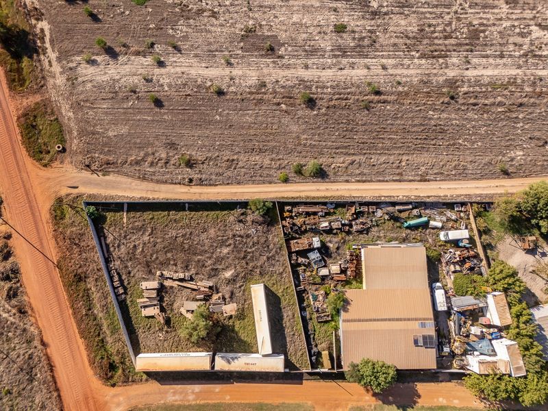 Aerial view of a residential land plot featuring a metal-roofed structure, perimeter fencing, and significant accumulation of scrap materials on the site.