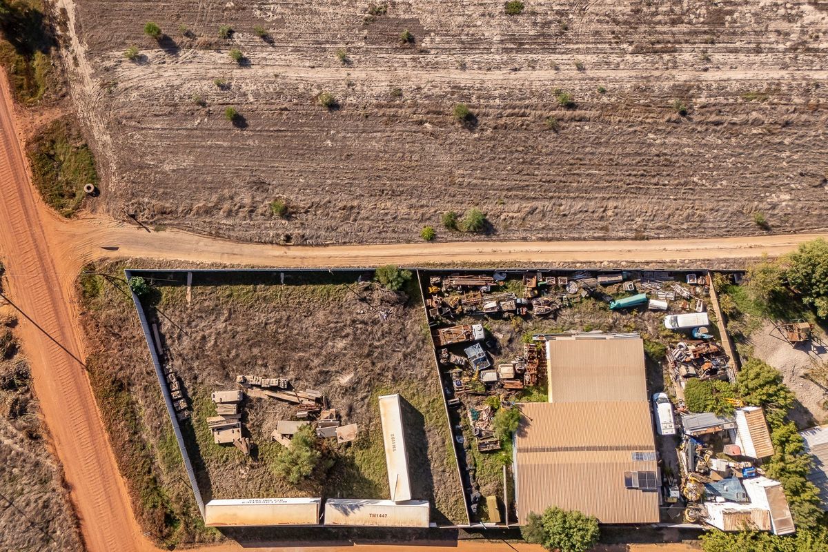 Aerial view of a residential land plot featuring a metal-roofed structure, perimeter fencing, and significant accumulation of scrap materials on the site.