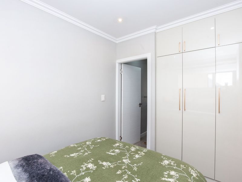 A clean, modern bedroom featuring high-gloss built-in cupboards with contemporary handles, recessed ceiling lighting, and elegant crown molding.