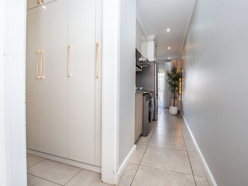 A modern galley-style kitchen featuring sleek built-in cabinetry, tiled flooring, and integrated appliances, leading towards a bright living area.