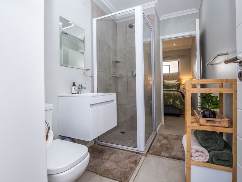 Modern bathroom featuring a glass-enclosed shower, wall-mounted vanity with basin, and toilet, finished with neutral floor and wall tiles.