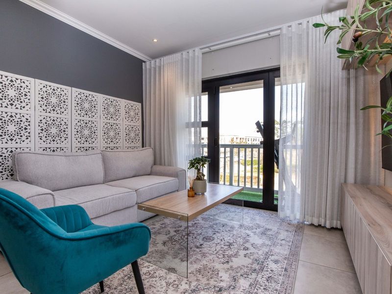 A well-maintained living room featuring tiled flooring, recessed lighting, crown molding, and a sliding glass door providing access to a balcony.