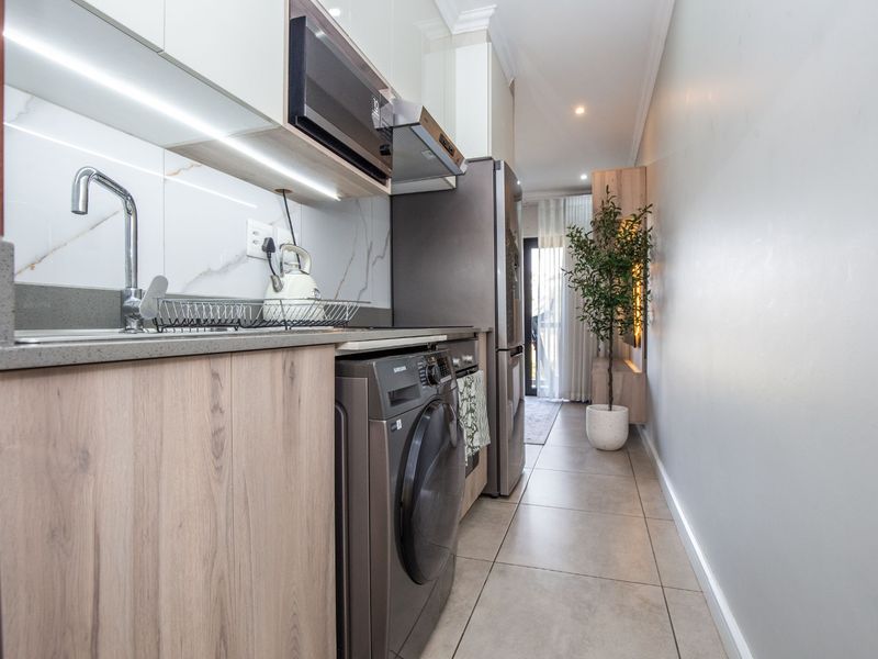 Modern galley-style kitchen featuring sleek wood-grain cabinetry, stone countertops, integrated appliances, and high-quality marble-look splashback with ambient under-cabinet lighting.