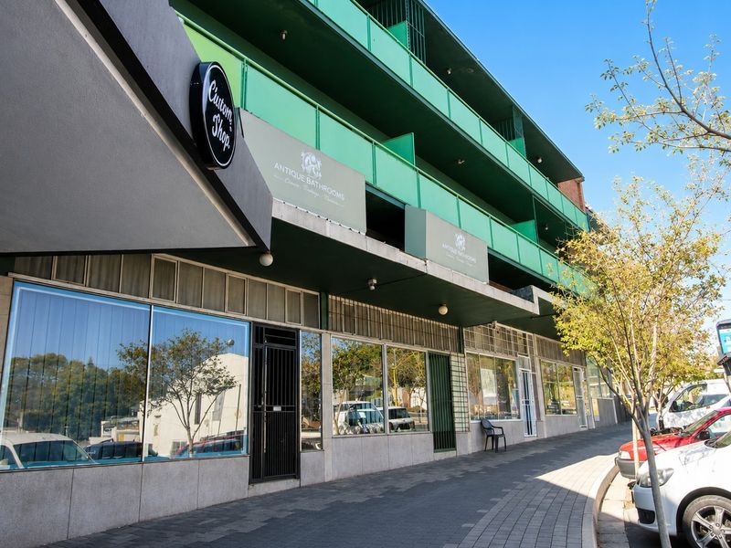 Street-level view of a commercial building featuring large display windows, a secure entrance, and an upper-level balcony with green metal railings.