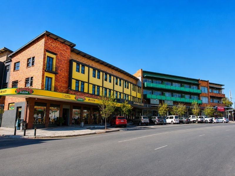 A multi-story commercial building featuring brick and yellow facade elements, ground-floor retail storefronts, and upper-level balconies along a street-facing frontage.