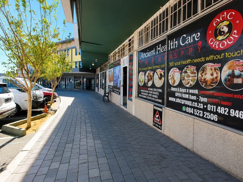 Front exterior view of a commercial storefront featuring a paved walkway, overhead awning, and prominent business signage.