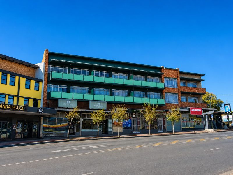 Street-level view of a multi-story commercial building featuring brick facade, ground-floor retail storefronts, and upper-level balconies.