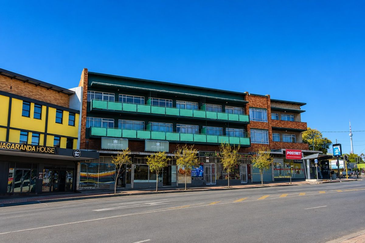 Street-level view of a multi-story commercial building featuring brick facade, ground-floor retail storefronts, and upper-level balconies.