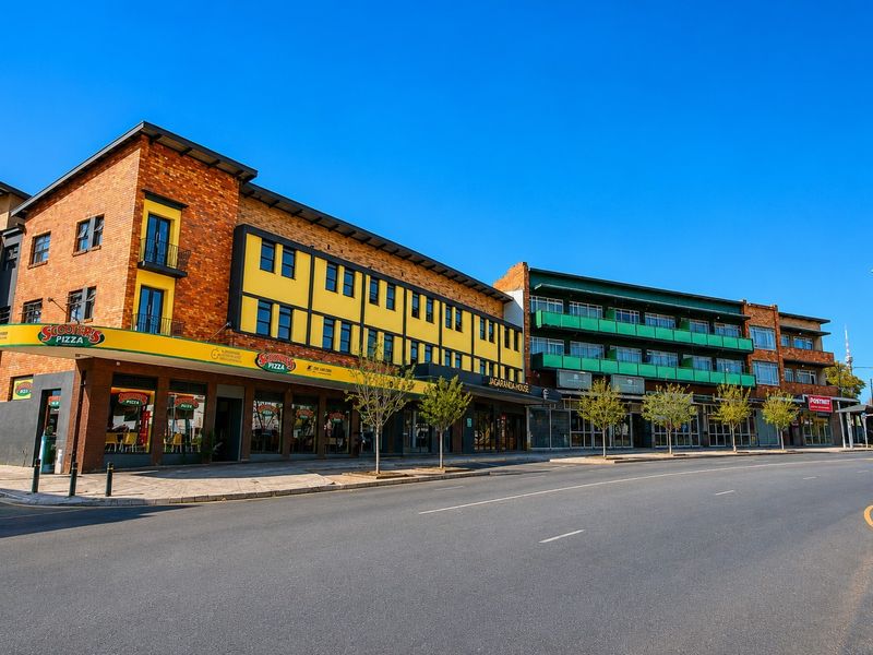 A well-maintained commercial building complex featuring brick facades, multiple storefronts, and upper-level balconies along a paved street.