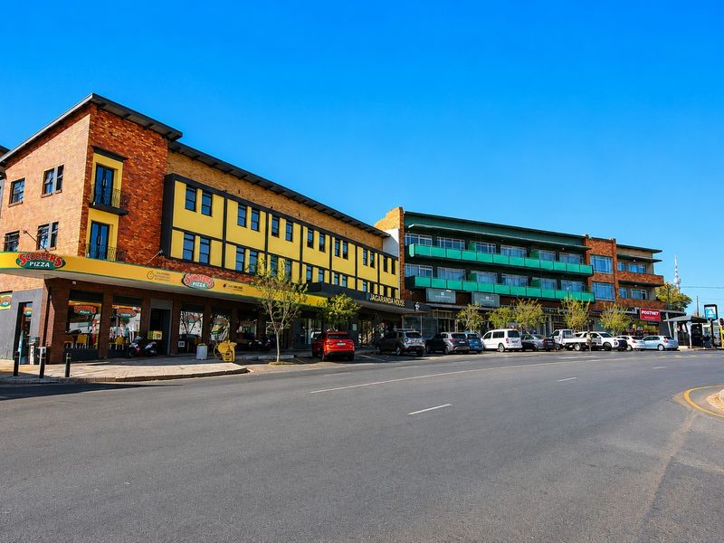 A street-level view of a multi-story commercial building featuring brick and yellow facade elements, ground-floor retail spaces, and upper-level balconies.