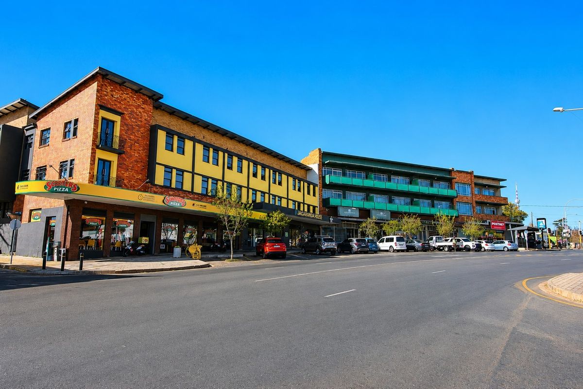 A street-level view of a multi-story commercial building featuring brick and yellow facade elements, ground-floor retail spaces, and upper-level balconies.