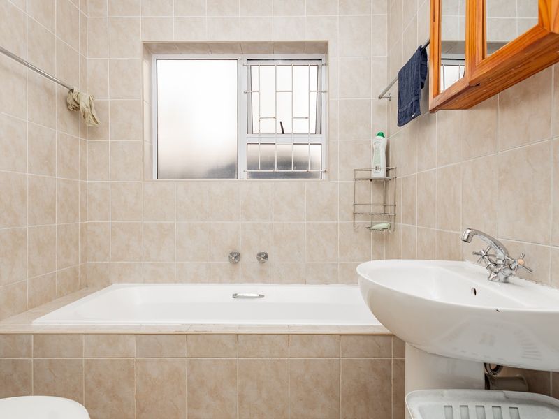 A functional bathroom featuring a built-in bathtub, pedestal basin, and neutral wall tiling, offering a clean space with potential for modern updates.