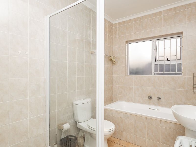 A functional bathroom featuring a shower enclosure, bathtub, pedestal basin, and neutral wall tiling, offering a practical layout with potential for modern updates.