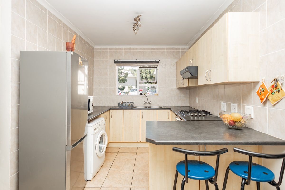 A functional kitchen featuring light wood cabinetry, dark laminate countertops, a gas hob with extractor, and a convenient breakfast bar area.