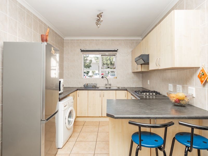 A functional kitchen featuring light wood cabinetry, dark laminate countertops, a gas hob with extractor, and a convenient breakfast bar area.