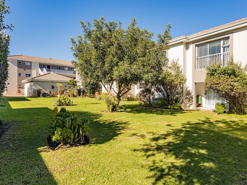 A well-maintained communal garden area featuring lush green lawns, mature trees, and access to apartment balconies.