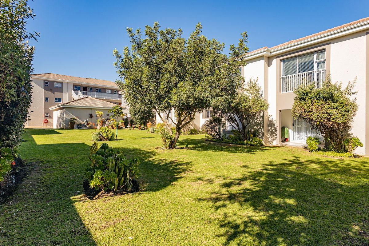A well-maintained communal garden area featuring lush green lawns, mature trees, and access to apartment balconies.