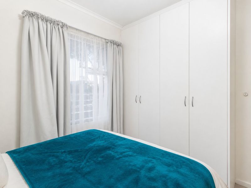 A bright bedroom featuring clean white built-in cupboards and a window with neutral curtains.