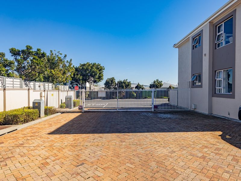 A well-maintained apartment complex entrance featuring a paved driveway, secure perimeter fencing, and a gated access point.