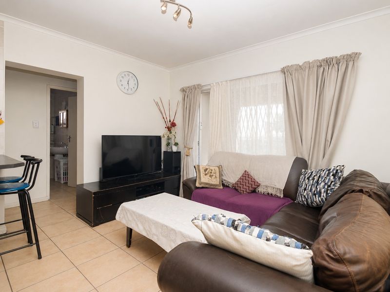 A living room featuring tiled flooring, a sliding glass door with security gate, and access to an adjacent bathroom area.
