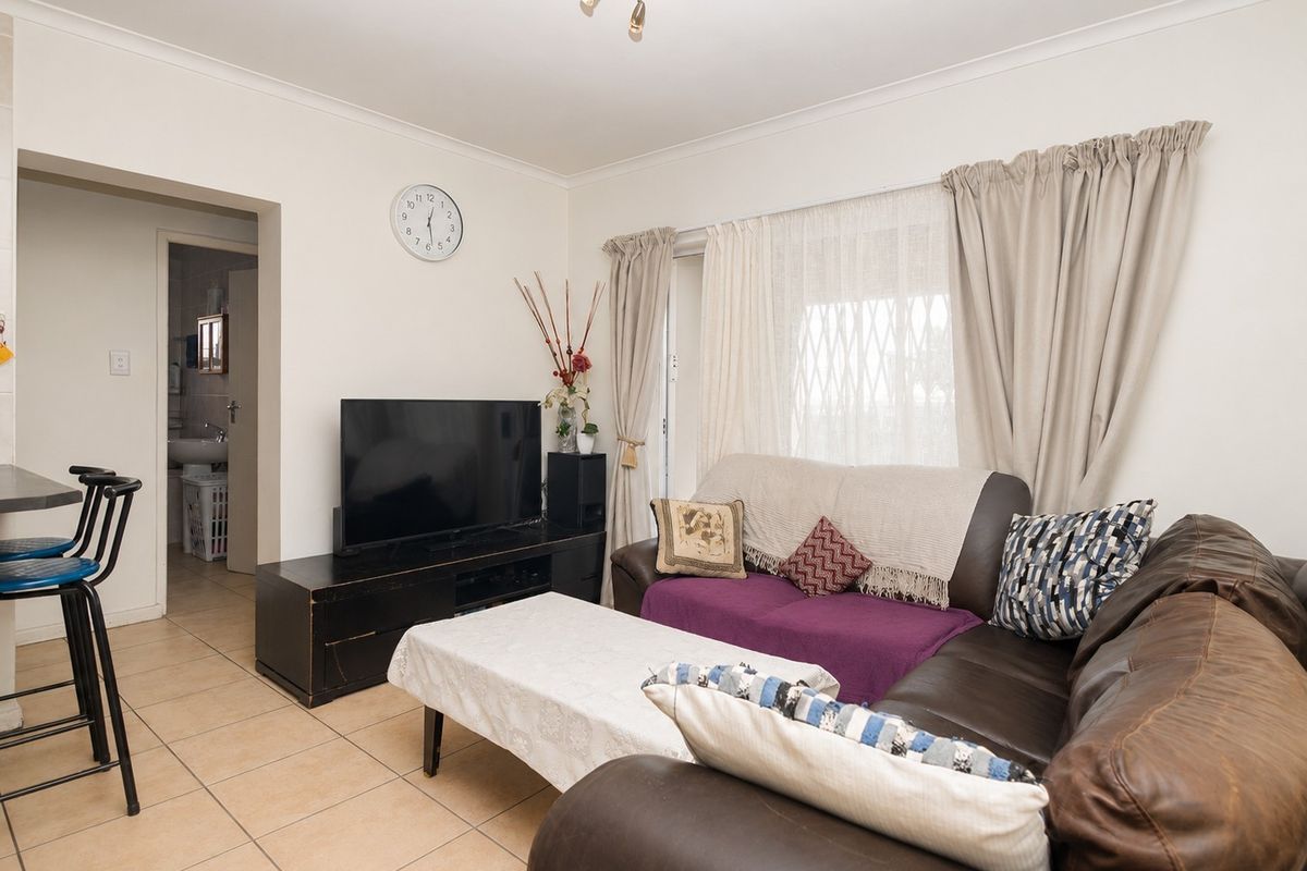 A living room featuring tiled flooring, a sliding glass door with security gate, and access to an adjacent bathroom area.