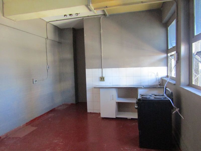 A basic, empty kitchen area featuring a stainless steel sink, tiled splashback, and exposed electrical conduit, requiring significant renovation and modernization.