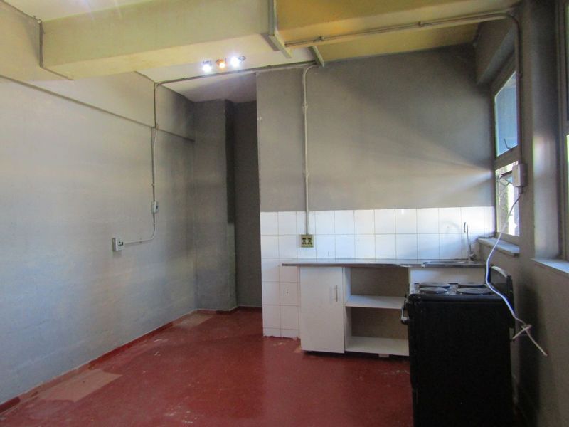 A basic, empty kitchen area featuring a small sink unit, tiled splashback, and exposed structural and electrical elements, offering potential for renovation.