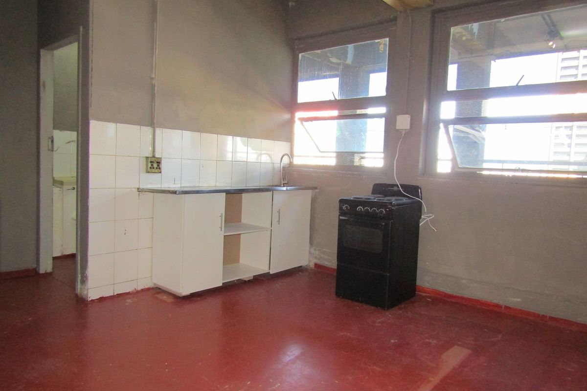 A basic, unfinished kitchen area featuring a small sink unit, tiled splashback, and a freestanding stove, requiring significant renovation and cosmetic updates.
