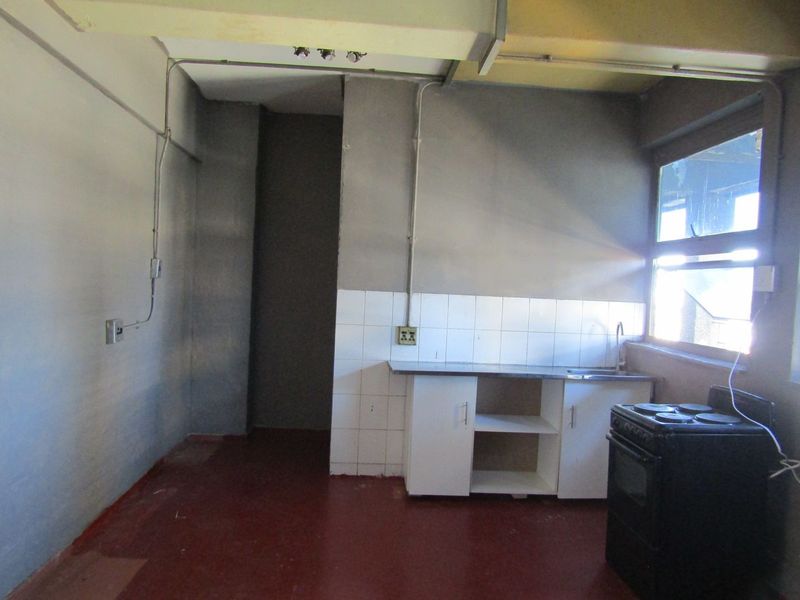 A basic, empty kitchen area featuring a sink, tiled splashback, and base cabinetry, requiring significant renovation and cosmetic updates.