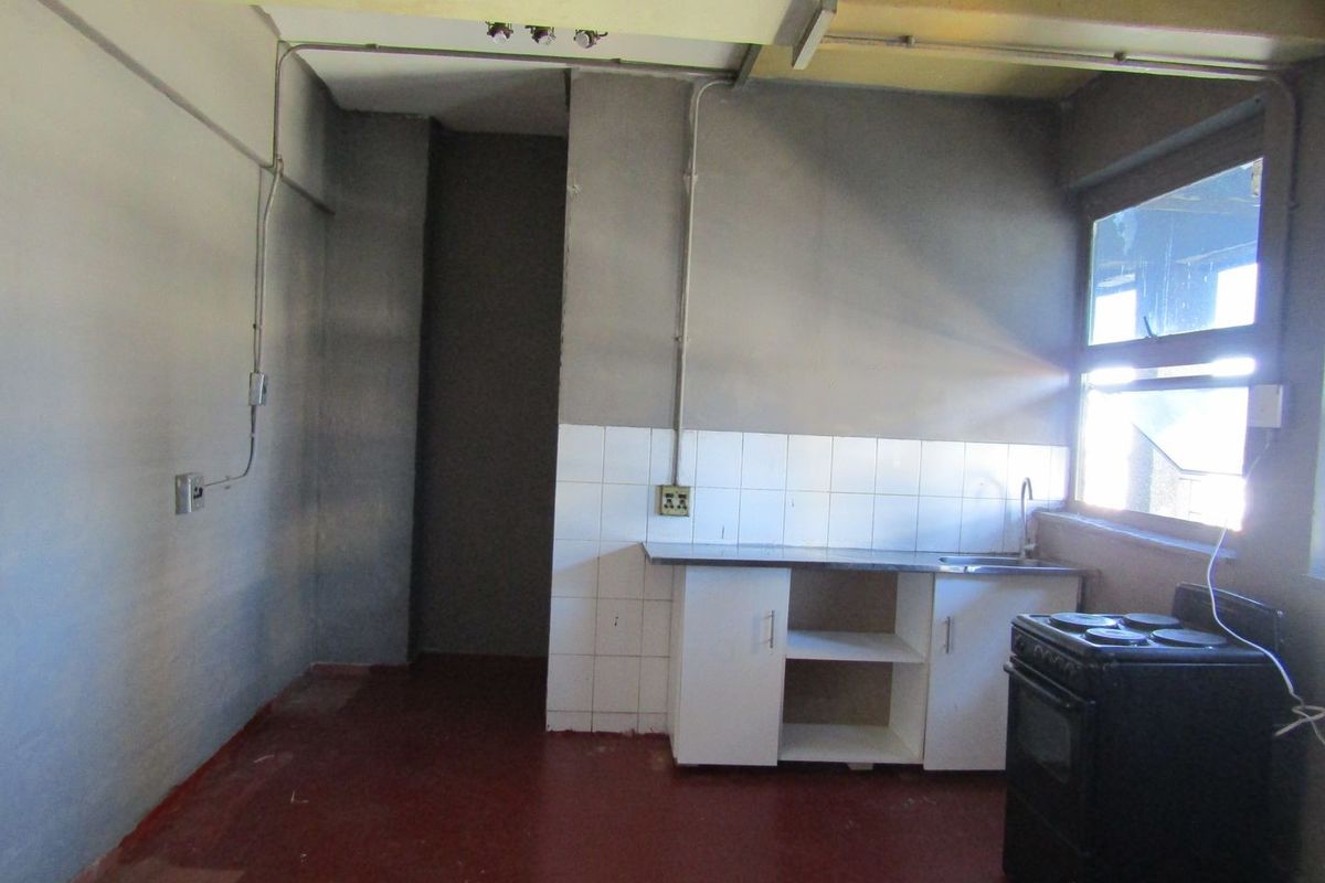 A basic, empty kitchen area featuring a sink, tiled splashback, and base cabinetry, requiring significant renovation and cosmetic updates.
